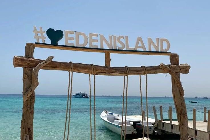Eden Island sign above the beach swings, with the jetty and turquoise sea behind