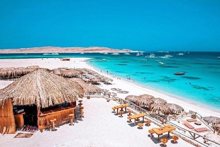 Thatched huts on the white sand of Eden Island above clear turquoise water and moored day boats