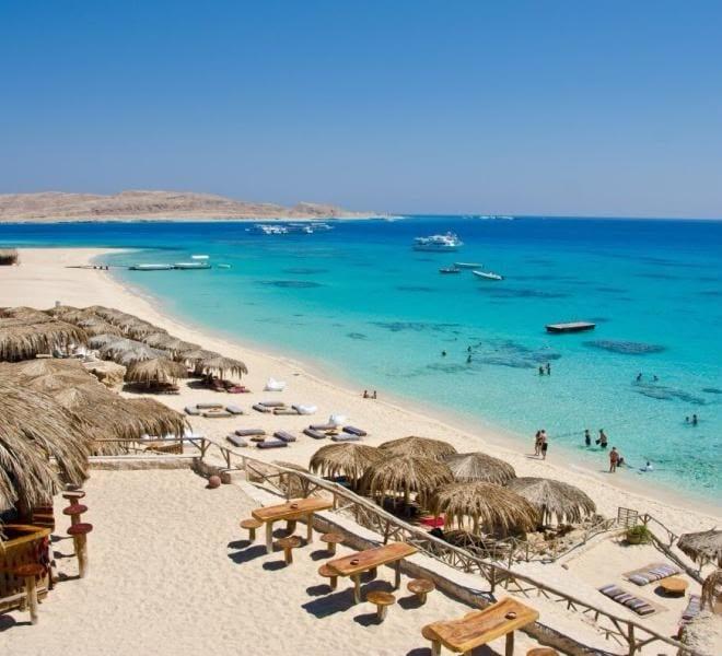 Straw parasols along the beach and boats in the turquoise lagoon at Mahmya