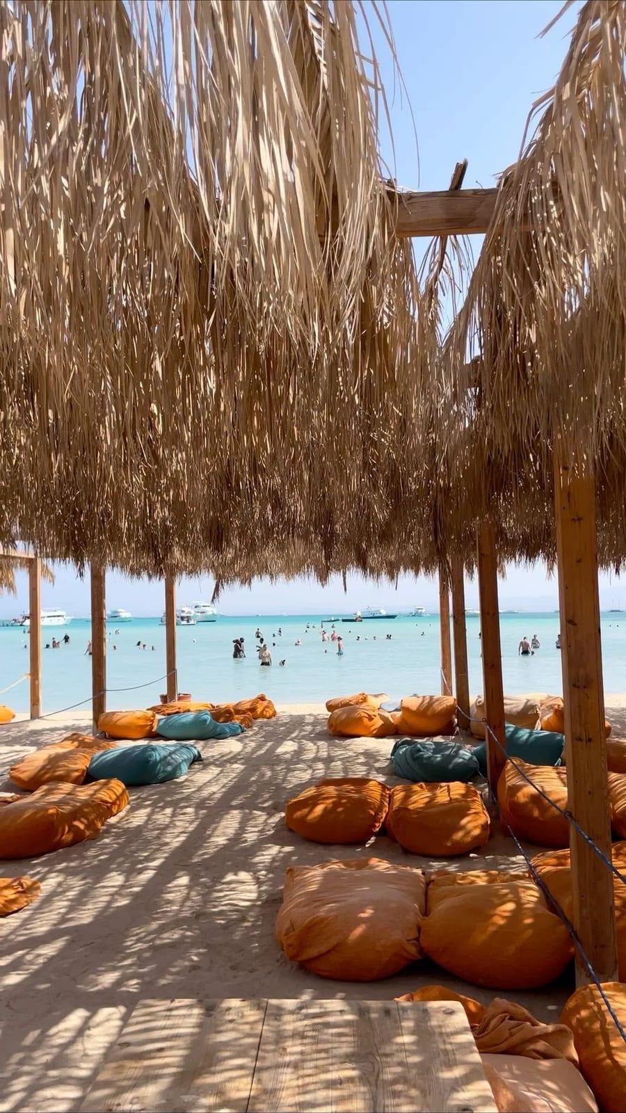 Beanbags in the shade of straw parasols facing the water at Orange Bay