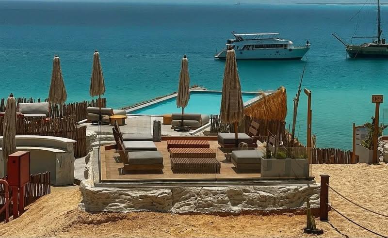 Beach lounge and straw parasols overlooking boats in the turquoise water at Ozirea Island