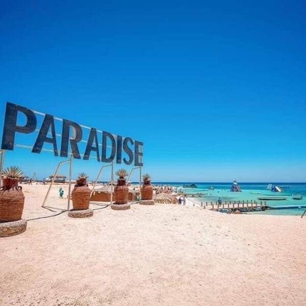 Large Paradise letters on the beach with parasols behind