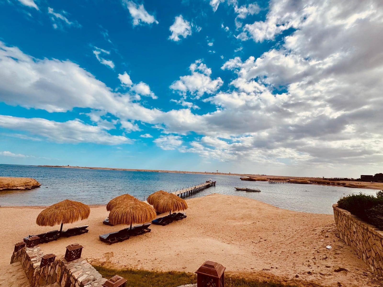 Straw umbrellas and loungers on the sandy beach of Sharm El Naga with its wooden pier